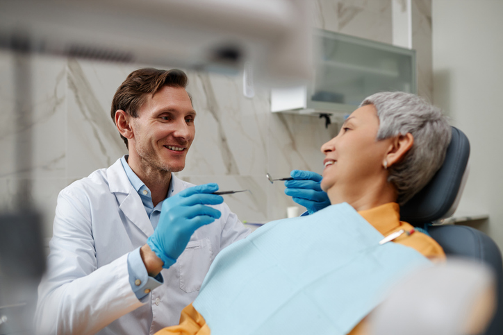 Smiling male dentist examining senior woman during dental checkup at clinic